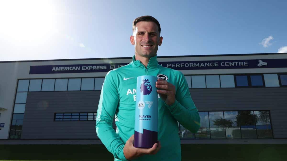 Pascal Groß sonríe con el trofeo de Jugador del Mes de la Premier League frente al centro de entrenamiento de Brighton