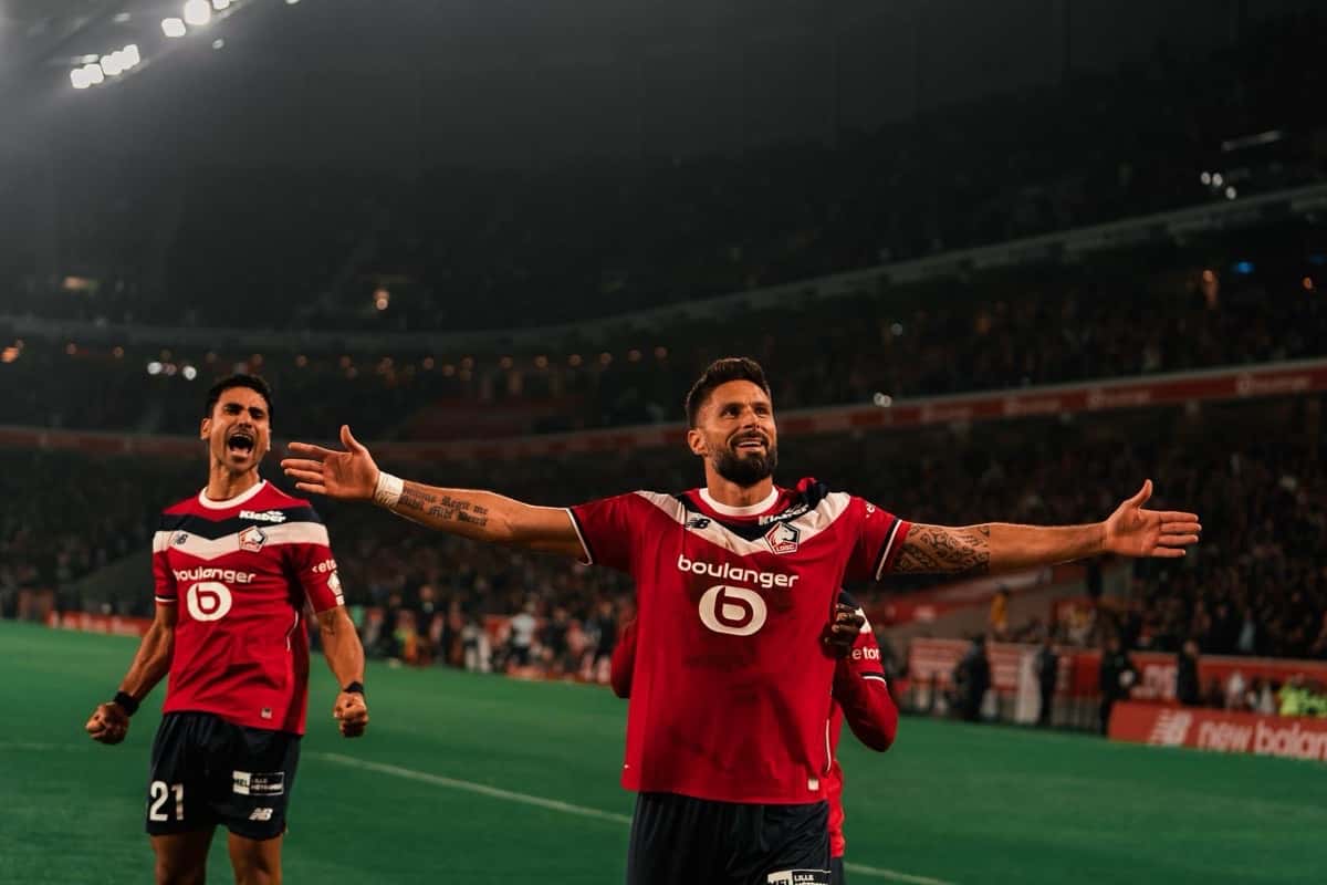 Olivier Giroud, con la camiseta roja del Lille, abre los brazos para festejar su gol a Lens junto a un compañero, con las tribunas del Pierre-Mauroy de fondo, el viernes 30 de octubre (foto: LOSC)