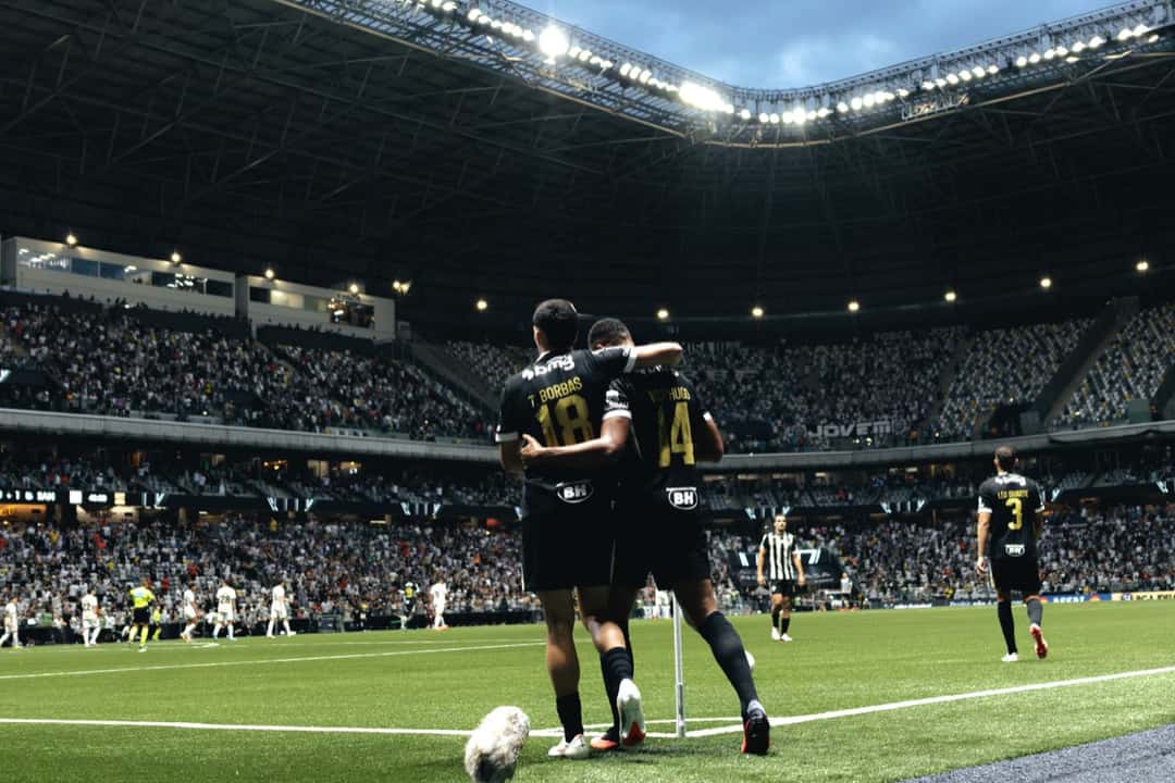 Thiago Borbas y un compañero de Atlético Mineiro, con la camiseta negra, se abrazan junto al banderín del córner tras uno de los goles del 2-1 a Santos en la Arena MRV, con las tribunas llenas de fondo (foto: Pedro Souza / prensa oficial de Atlético Mineiro)