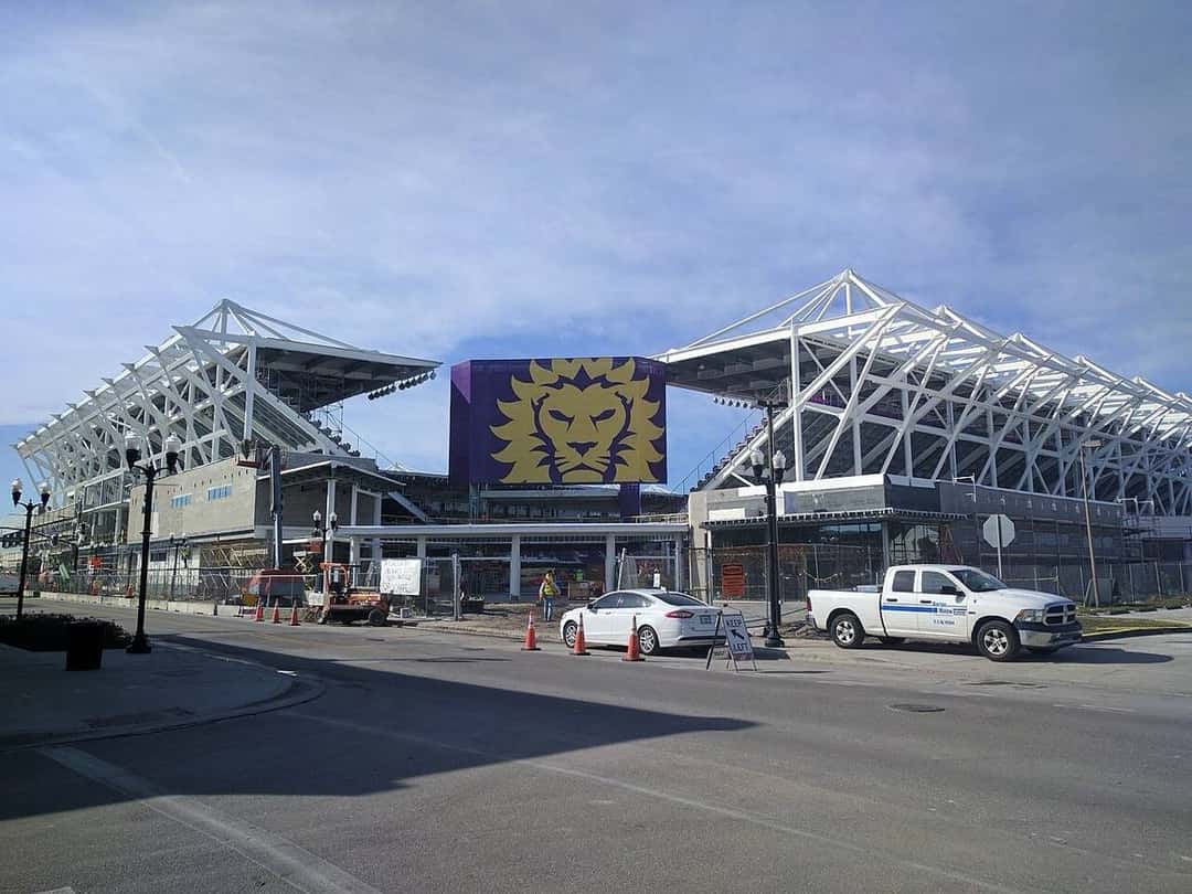 El exterior del estadio de Orlando City, con el escudo del león violeta en la fachada y la estructura blanca del techo; foto de archivo (foto: elisfkc, Wikimedia Commons, licencia CC BY-SA 2.0)