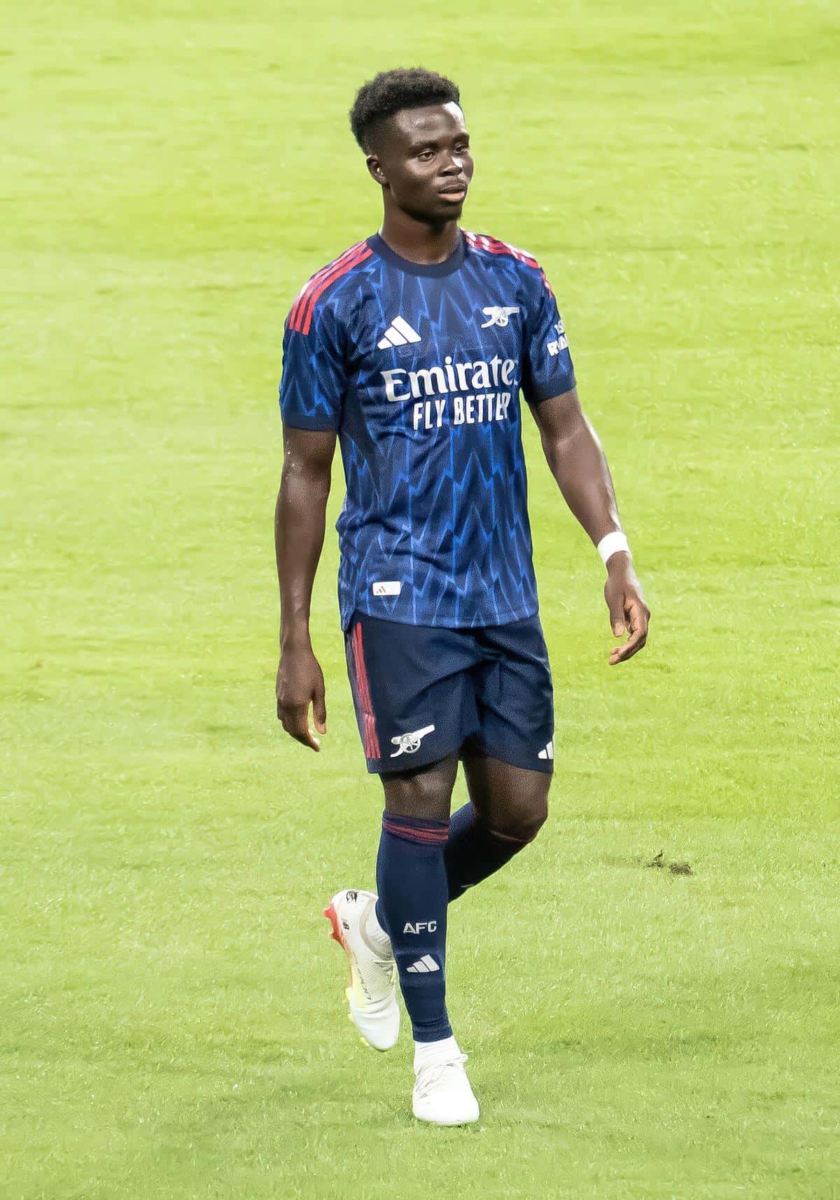 Bukayo Saka, con la camiseta azul oscuro del Arsenal de la temporada 2025-26, camina por el campo durante un amistoso de pretemporada; foto de archivo de julio de 2025 (foto: Chensiyuan, Wikimedia Commons, licencia CC BY-SA 4.0)