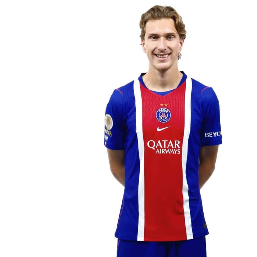Mika Godts, sonriente y con la camiseta azul y roja del PSG de la temporada 2026-27, en la foto oficial del plantel (foto: Paris Saint-Germain)