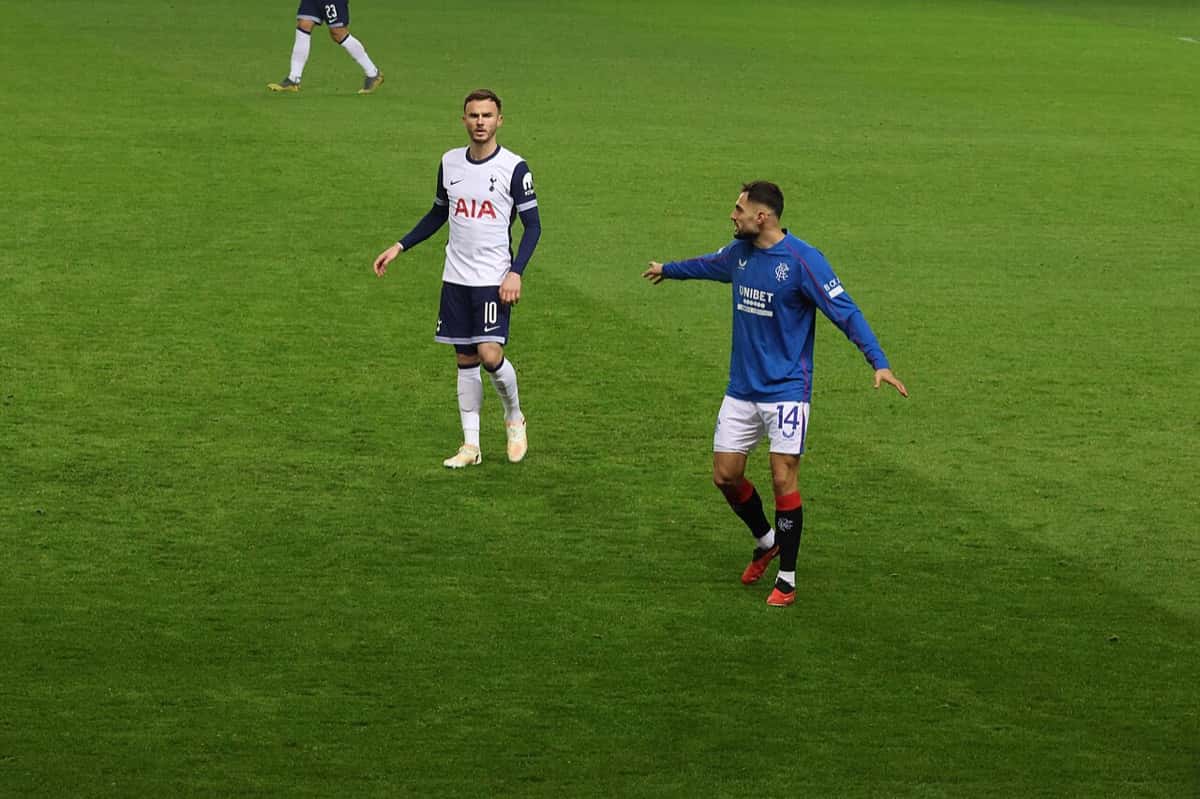 James Maddison, con la camiseta blanca número 10 de Tottenham, camina por el campo junto a un jugador de Rangers de azul durante un partido de la Europa League; foto de archivo de diciembre de 2024 (foto: Jim Easton, Wikimedia Commons, dominio público CC0)