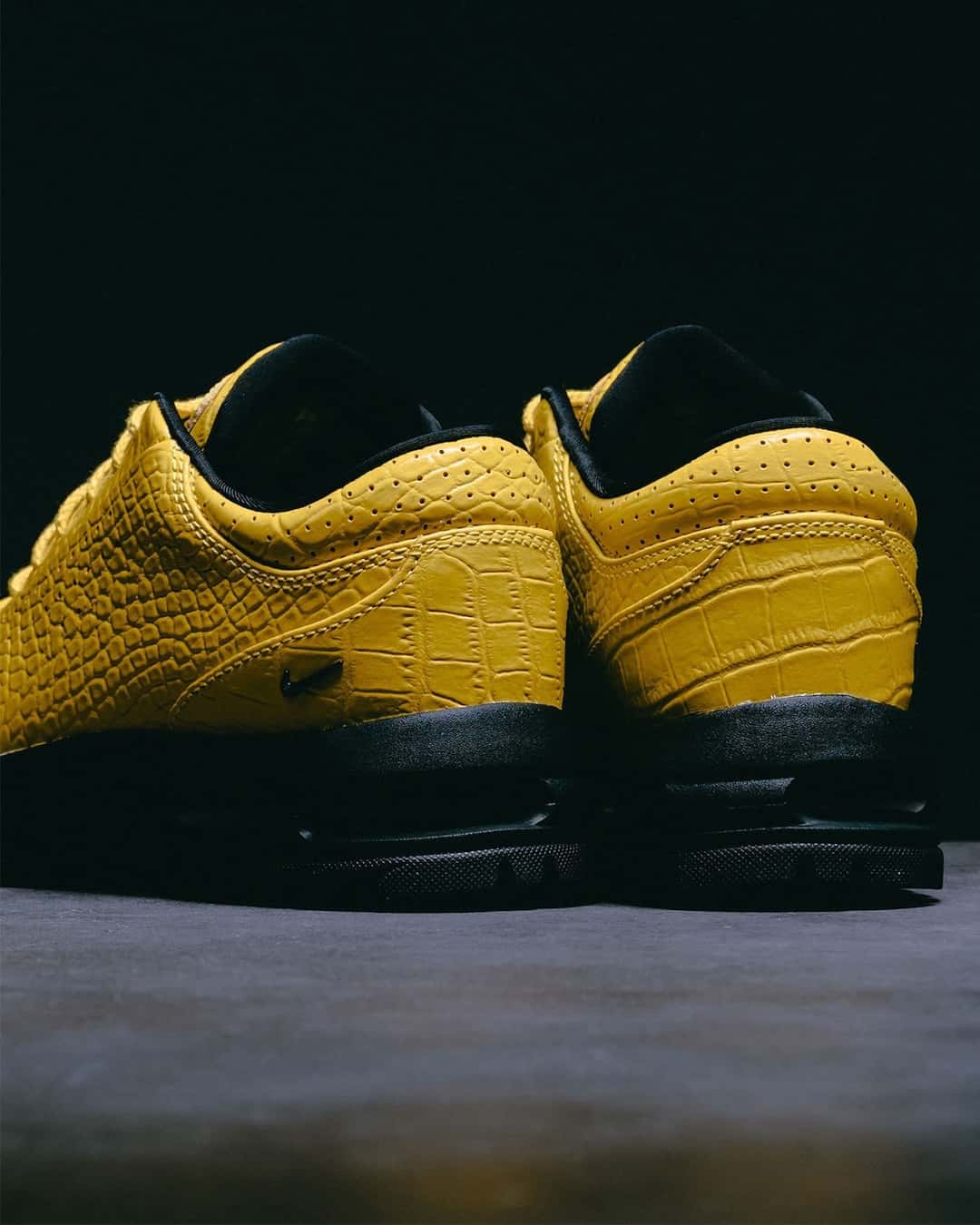 Vista trasera del par del Nike Air Max Goadome Low Yellow Croc, con el talón de cuero amarillo grabado tipo cocodrilo, perforaciones en el cuello, borde negro en la boca de la zapatilla y base negra con la unidad Air a la vista