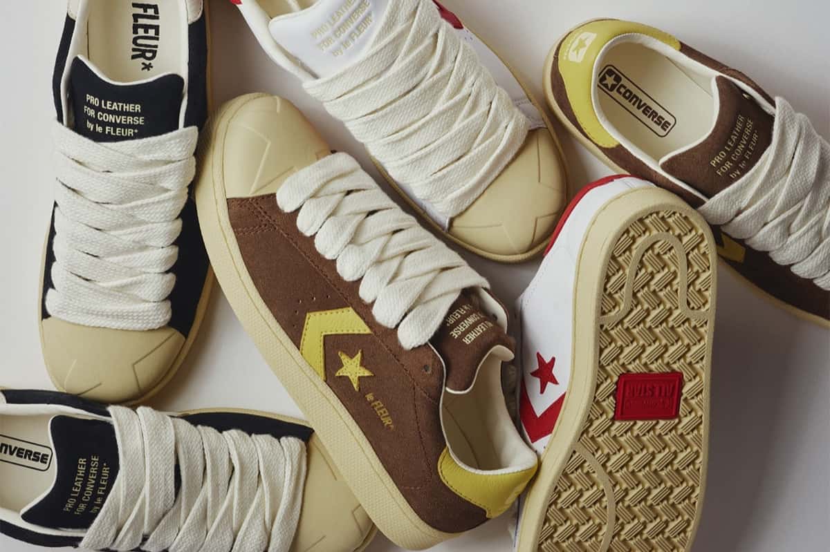 Varios pares de la Converse Pro Leather de GOLF le FLEUR* apilados sobre fondo blanco: uno de gamuza marrón con la estrella y el chevron amarillos, uno blanco con detalles rojos, uno negro, todos con cordones gruesos color crudo, puntera de goma y la leyenda Pro Leather for Converse by le FLEUR* en la lengüeta