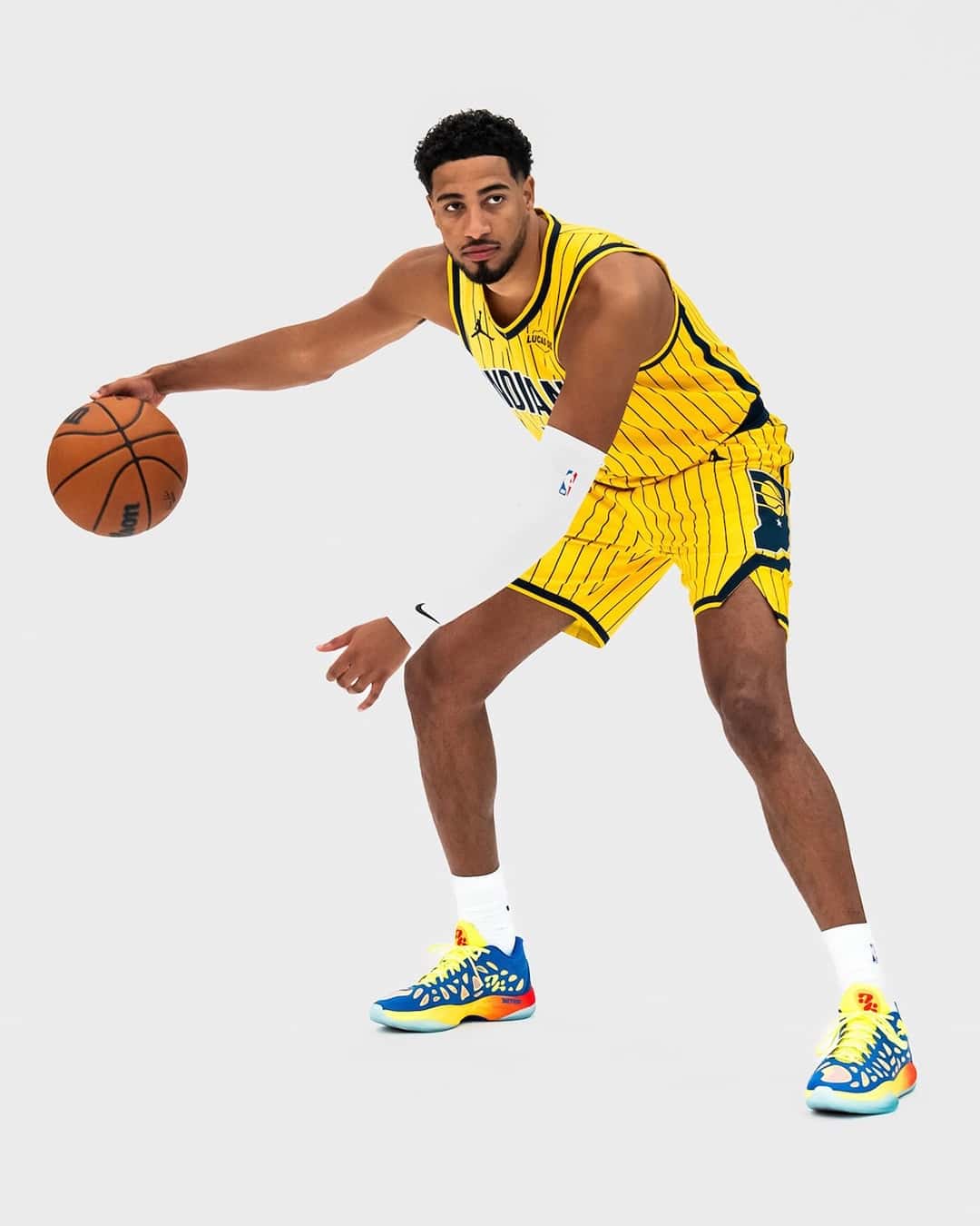 Tyrese Haliburton con la camiseta amarilla a rayas de los Indiana Pacers picando una pelota de básquet en una foto de estudio, con las PUMA Hali 2 Thermal Vision puestas