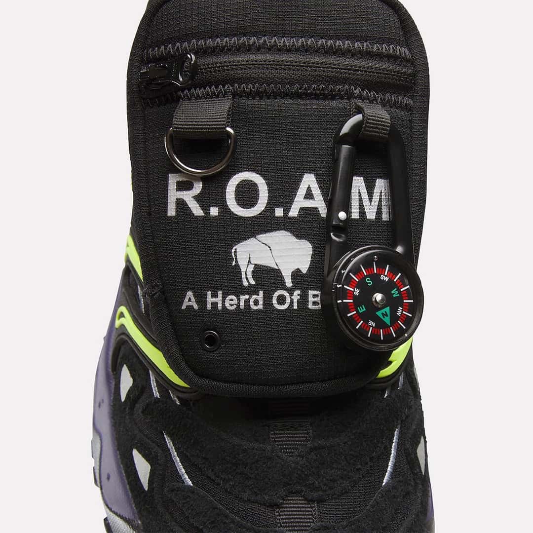 Primer plano del bolsillo de la Reebok DMX Trailzillo de A Herd of Bison, negro con la inscripción R.O.A.M, el bisonte y una brújula colgada de un mosquetón
