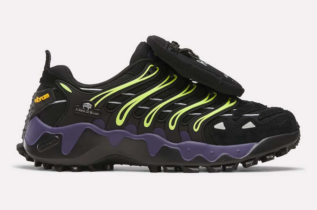 Reebok DMX Trailzillo de A Herd of Bison de perfil sobre fondo gris claro, negra con líneas verde lima, logo Vibram naranja en el costado y entresuela violeta con forma ondulada
