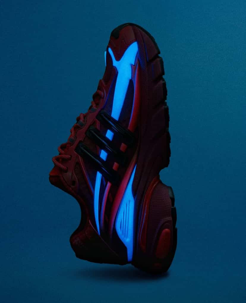 Pharrell x adidas Adistar Jellyfish Red de perfil sobre fondo azul oscuro, con las capas laterales que brillan en celeste en la oscuridad sobre la base roja
