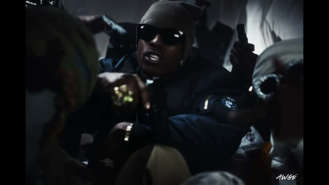 Fotograma del video oficial de «SWAT TEAM»: A$AP Rocky, con anteojos negros y gorro gris, en medio de un grupo de personas con chalecos, con poca luz
