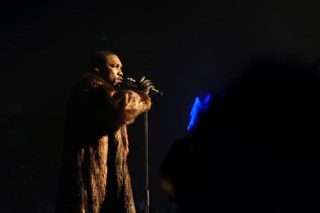 GIVĒON canta con un abrigo de piel marrón y guantes negros en el escenario del Montreux Jazz Festival, sobre un fondo oscuro (foto de archivo, julio de 2026). Foto: Janeirohy, CC BY-SA 4.0, vía Wikimedia Commons