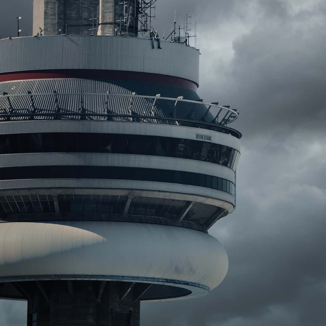 Portada de «VIEWS», de Drake: el artista sentado en el borde de la torre CN de Toronto, con un cielo gris y nublado de fondo
