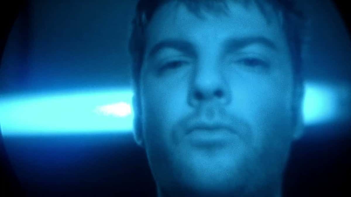 Fotograma del video oficial de «Tongue» de Fontaines D.C.: un hombre de pelo corto y barba corta mira a cámara bañado por una luz azul