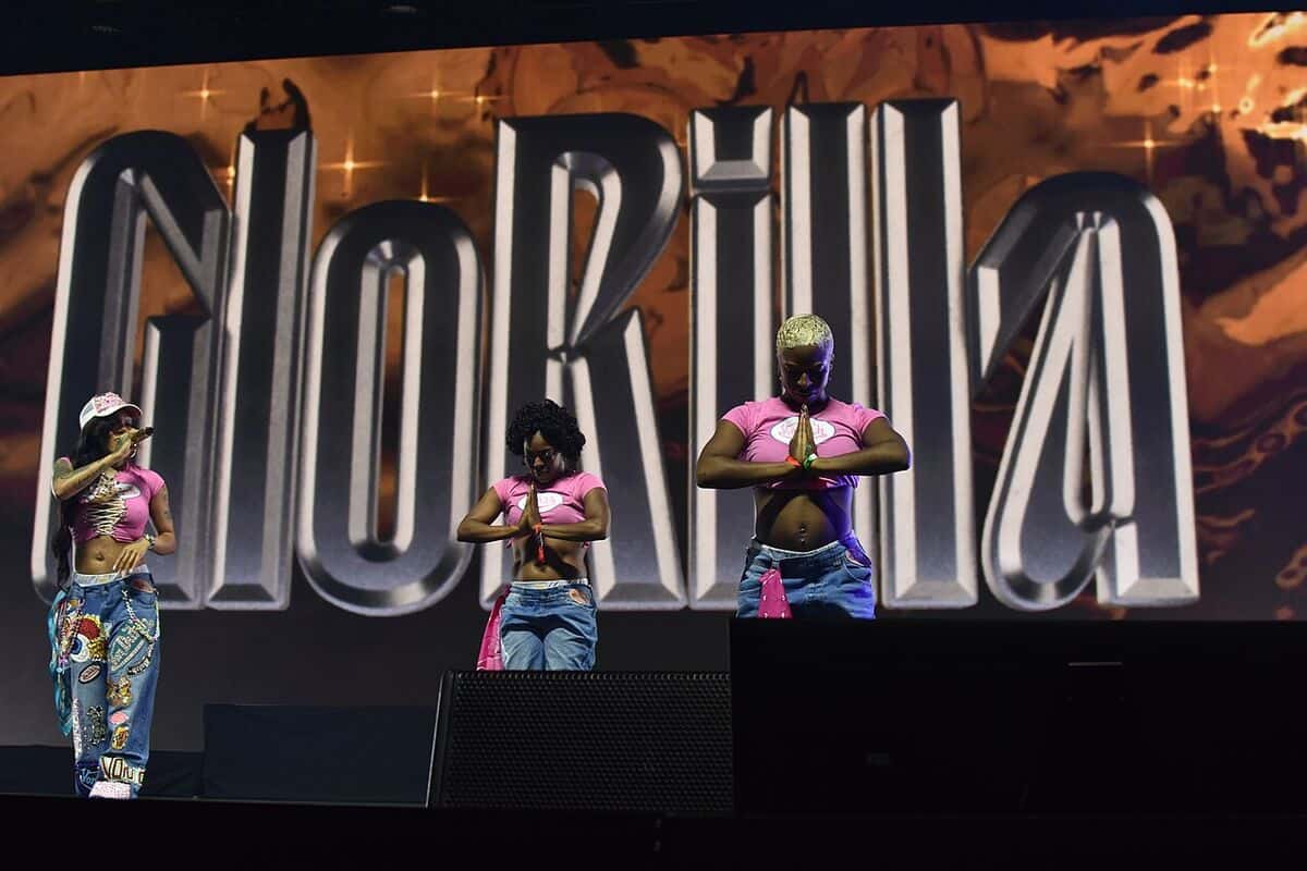 GloRilla con gorra, top rosa y jean estampado baila junto a dos bailarinas frente a una pantalla gigante con su nombre, en el Essence Fest 2025 (foto de archivo)