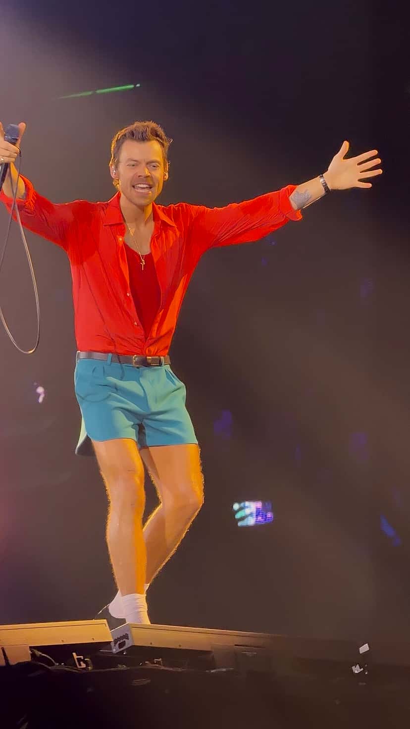 Harry Styles sonríe con los brazos abiertos y el micrófono en la mano, con camisa roja y short celeste, en el escenario del estadio de Wembley, en Londres (foto de archivo, junio de 2026). Foto: Wilnel José Verdú Guerrero, CC BY-SA 4.0, vía Wikimedia Commons