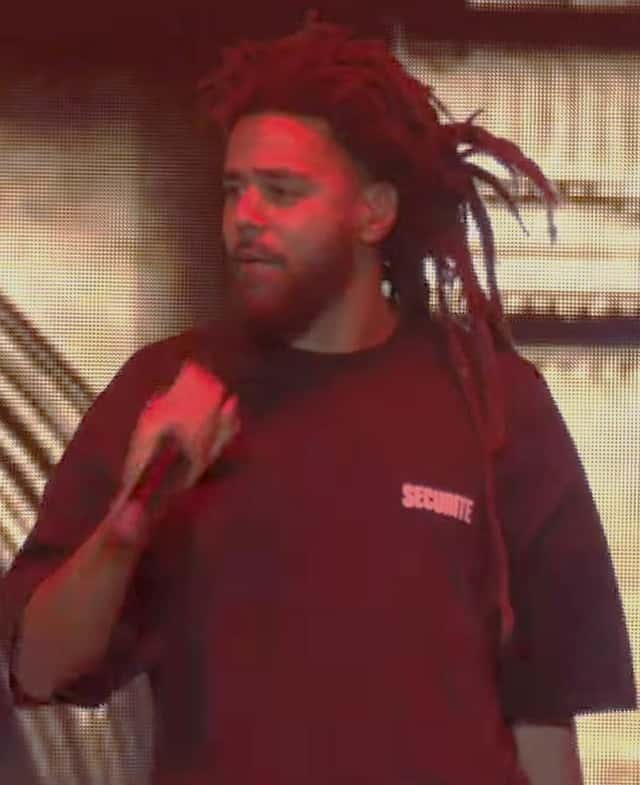 J. Cole canta con el micrófono en la mano, con remera bordó y el pelo largo, sobre un escenario, en junio de 2023 (foto de archivo). Foto: HOTSPOTATL, CC BY 3.0, vía Wikimedia Commons