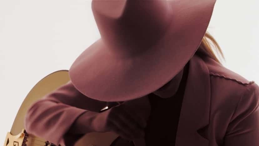 Lady Gaga con sombrero y saco bordó toca la guitarra en el video oficial de «Million Reasons» (fotograma del video oficial)