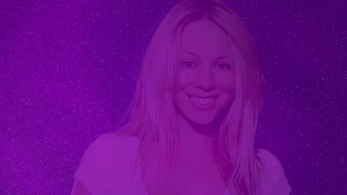 Mariah Carey, de pelo rubio largo y remera blanca, sonríe en una foto de la época de «Glitter» teñida de violeta, en una imagen del lyric video oficial de «Didn't Mean to Turn You On» con Rochelle Jordan