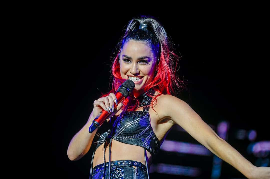 Lali sonriendo con un micrófono rojo en la mano, con el pelo atado y mechones rojos, durante un show en vivo (foto de archivo, 2023; Santiago Mazzarovich / Intendencia de Montevideo, CC BY-SA 4.0)