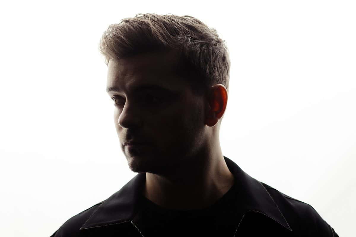 Foto de prensa de Martin Garrix: el DJ neerlandés de perfil, a contraluz, con el pelo corto peinado hacia arriba y camisa oscura, sobre un fondo blanco