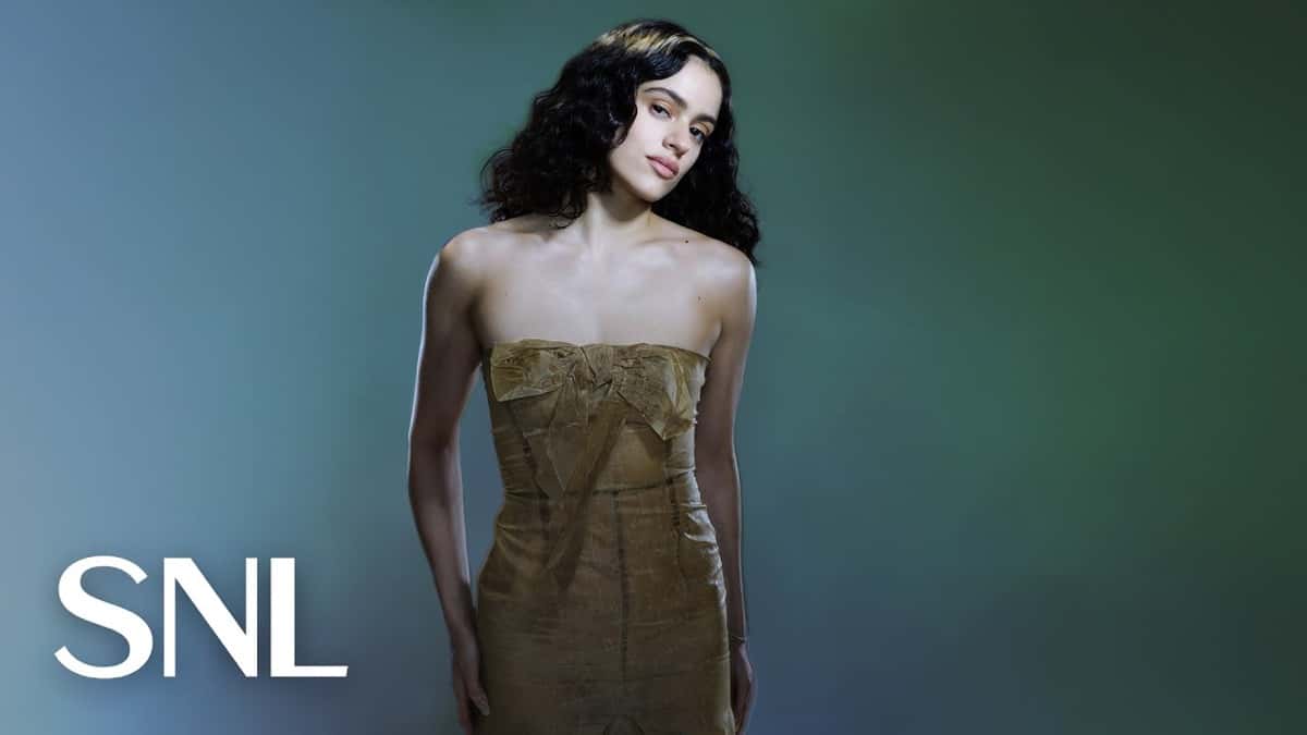 Retrato oficial de Rosalía para Saturday Night Live: la cantante posa con el pelo ondulado suelto y un vestido strapless dorado con un moño en el pecho, sobre un fondo verde azulado, con el logo de SNL abajo a la izquierda