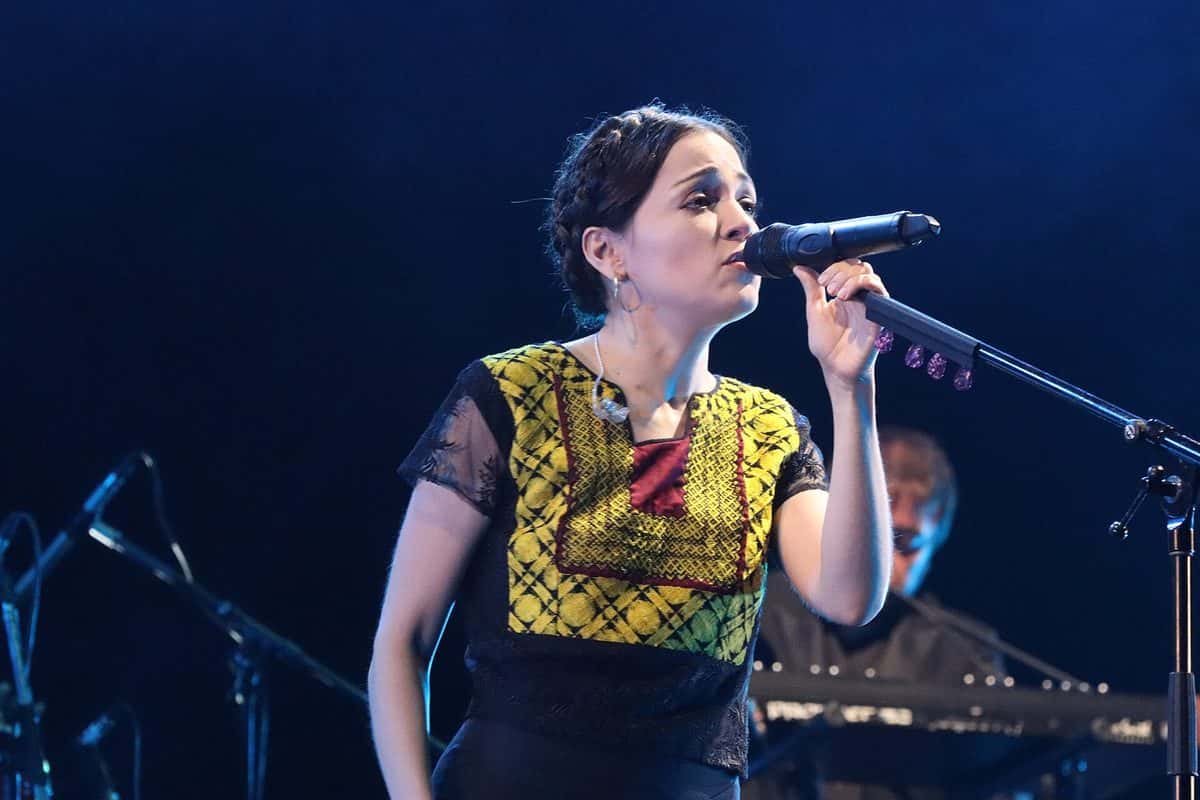 Natalia Lafourcade canta frente al micrófono con una blusa bordada amarilla y negra, iluminada en azul, durante un show en el teatro Gran Rex de Buenos Aires (foto de archivo, abril de 2018)