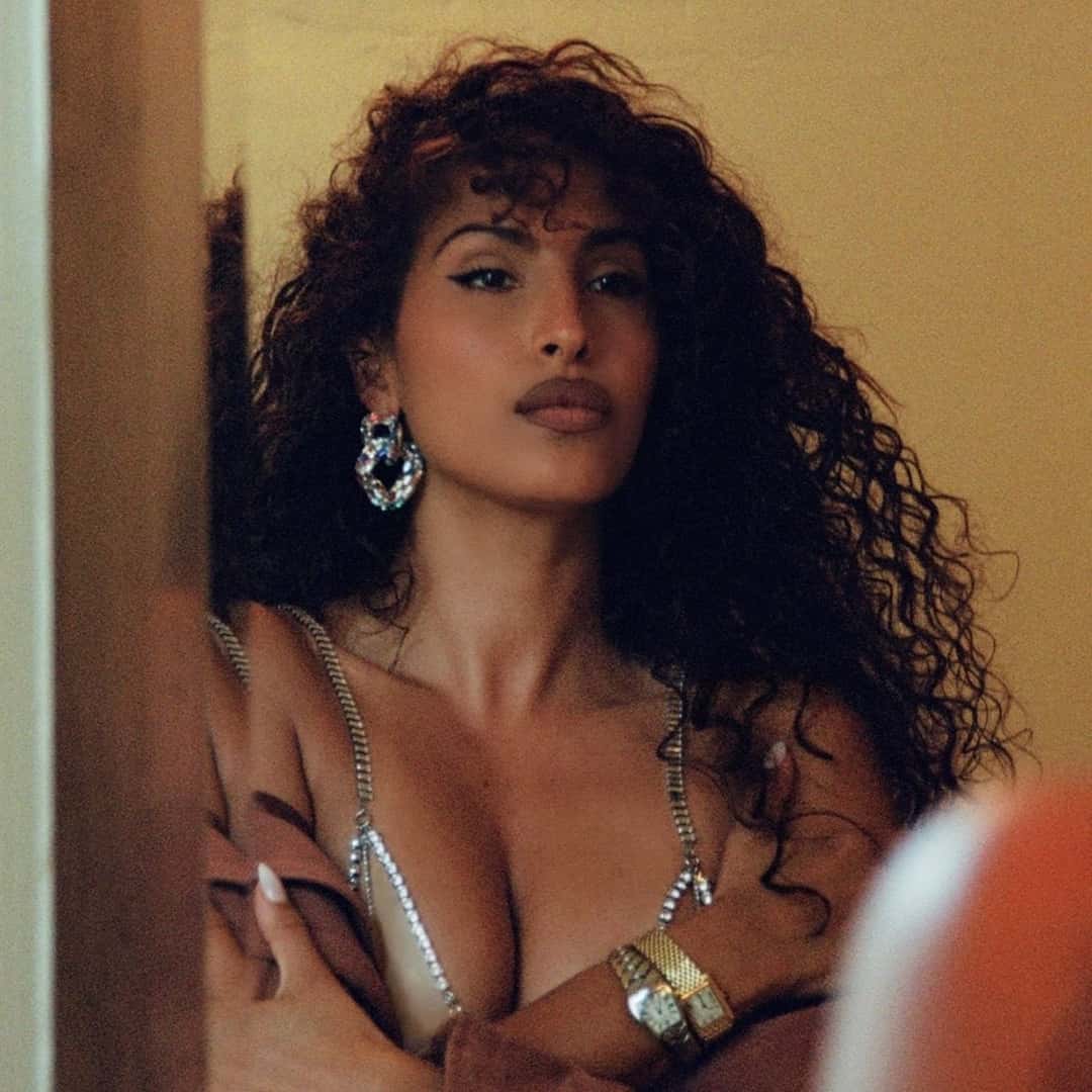 Portada oficial de «Legendary Love»: Snoh Aalegra, con pelo enrulado, aros grandes y brazaletes, apoyada en el marco de una puerta con los brazos cruzados, en tonos cálidos