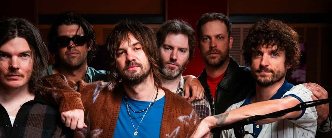 Kevin Parker, con campera marrón y remera azul, posa abrazado con los músicos de Tame Impala en el estudio de Like A Version, en una imagen oficial de la sesión