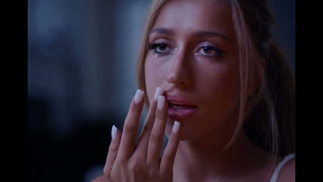 Fotograma del video oficial de «Housewife»: primer plano de Tate McRae con las uñas largas apoyadas cerca de la boca, en una escena con poca luz