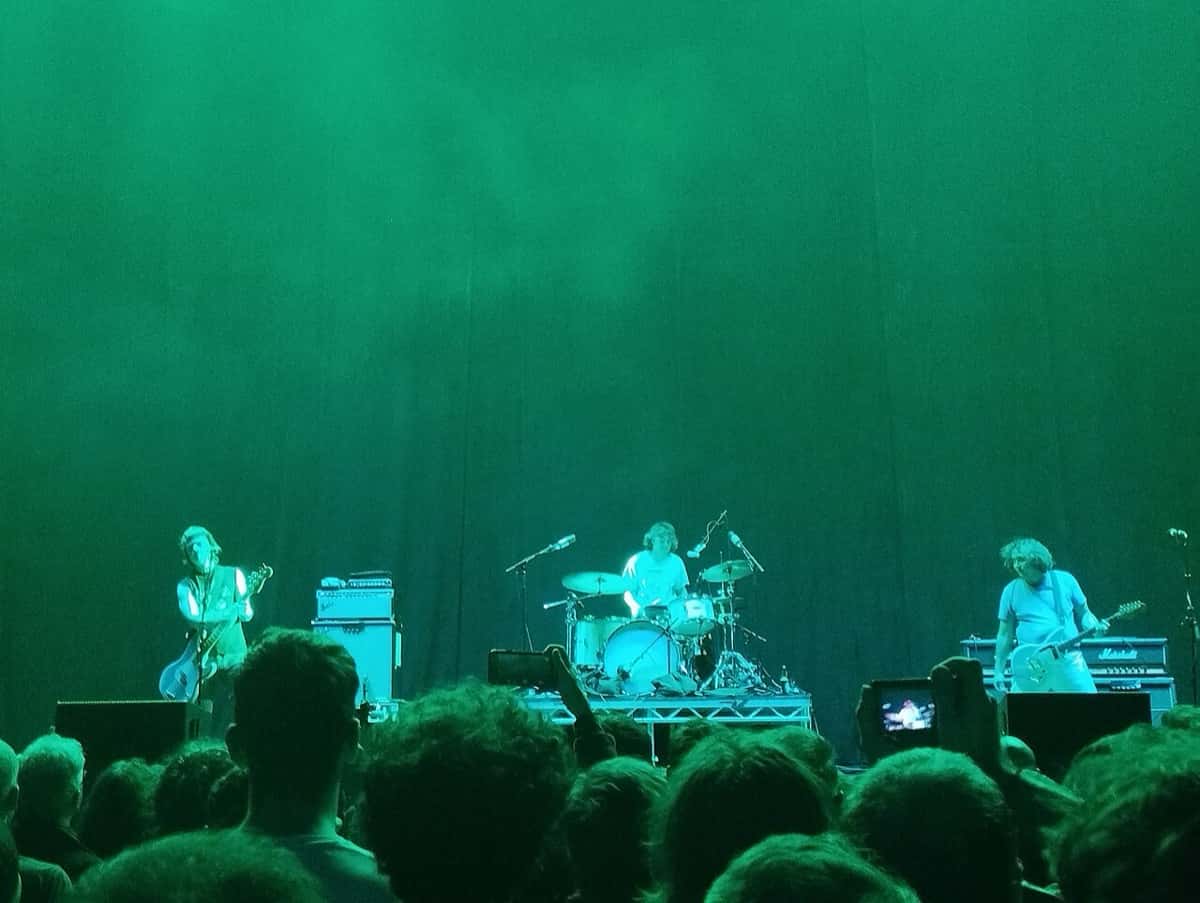 The Chats tocan en vivo con luz verde sobre un escenario grande, con el bajista y cantante a la izquierda, la batería al centro y el guitarrista a la derecha, frente al público, en el Accor Arena de París en 2023 (foto de archivo)