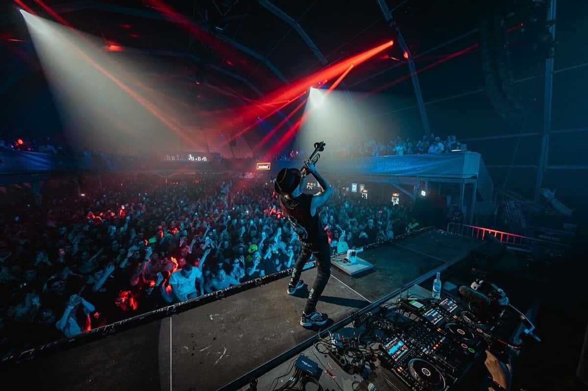 Timmy Trumpet en vivo en el SunIce Festival de 2023 (foto de archivo): de pie sobre la consola, con la trompeta en alto frente a un público enorme bajo luces rojas y azules