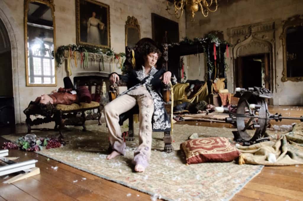 Troye Sivan sentado en un sillón tallado en el salón de un castillo, rodeado de invitados dormidos y restos de una fiesta, en una escena del video de Party