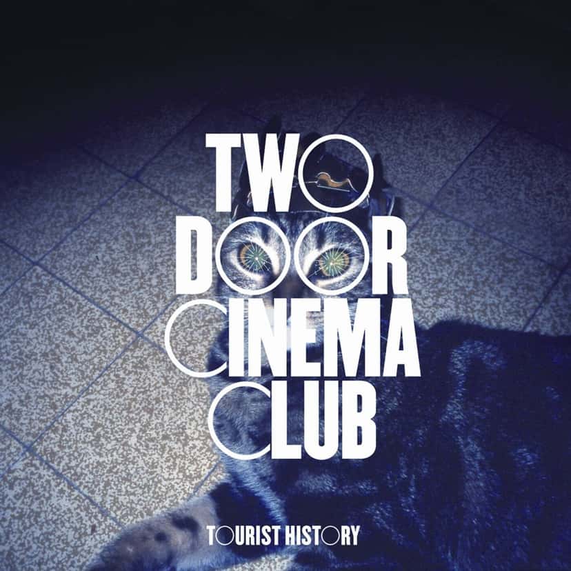 Portada de «Tourist History», el disco debut de Two Door Cinema Club: un gato sobre un piso de baldosas en tonos azules, con el nombre de la banda en letras blancas grandes