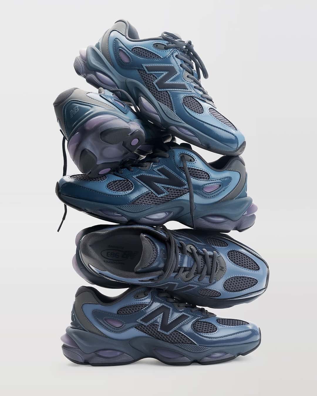 Pila de pares del New Balance 983 Shadow Blue mostrando los laterales, la plantilla con el logo 983 y los pods violetas de la mediasuela