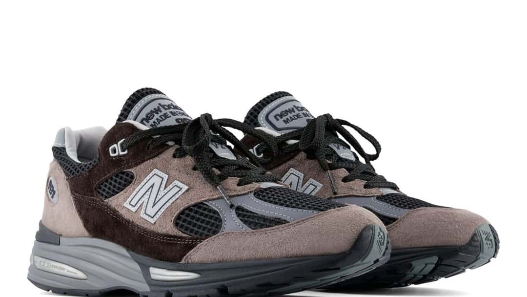 Par de New Balance 991v2 Iron/Mulch en vista lateral, con gamuza marrón, malla negra y entresuela gris