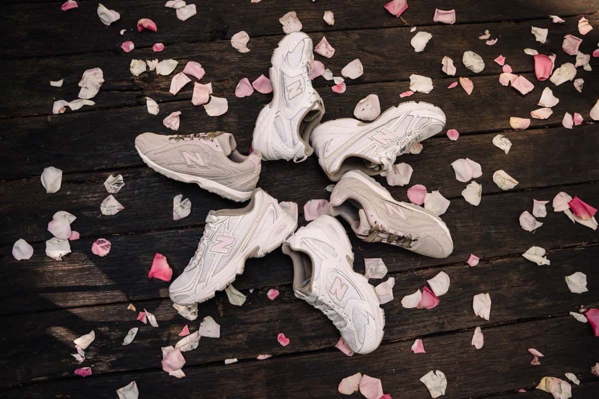 Varias zapatillas New Balance del Sakura Pack en tonos marfil y rosa, en ronda sobre un piso de madera con pétalos de flor de cerezo