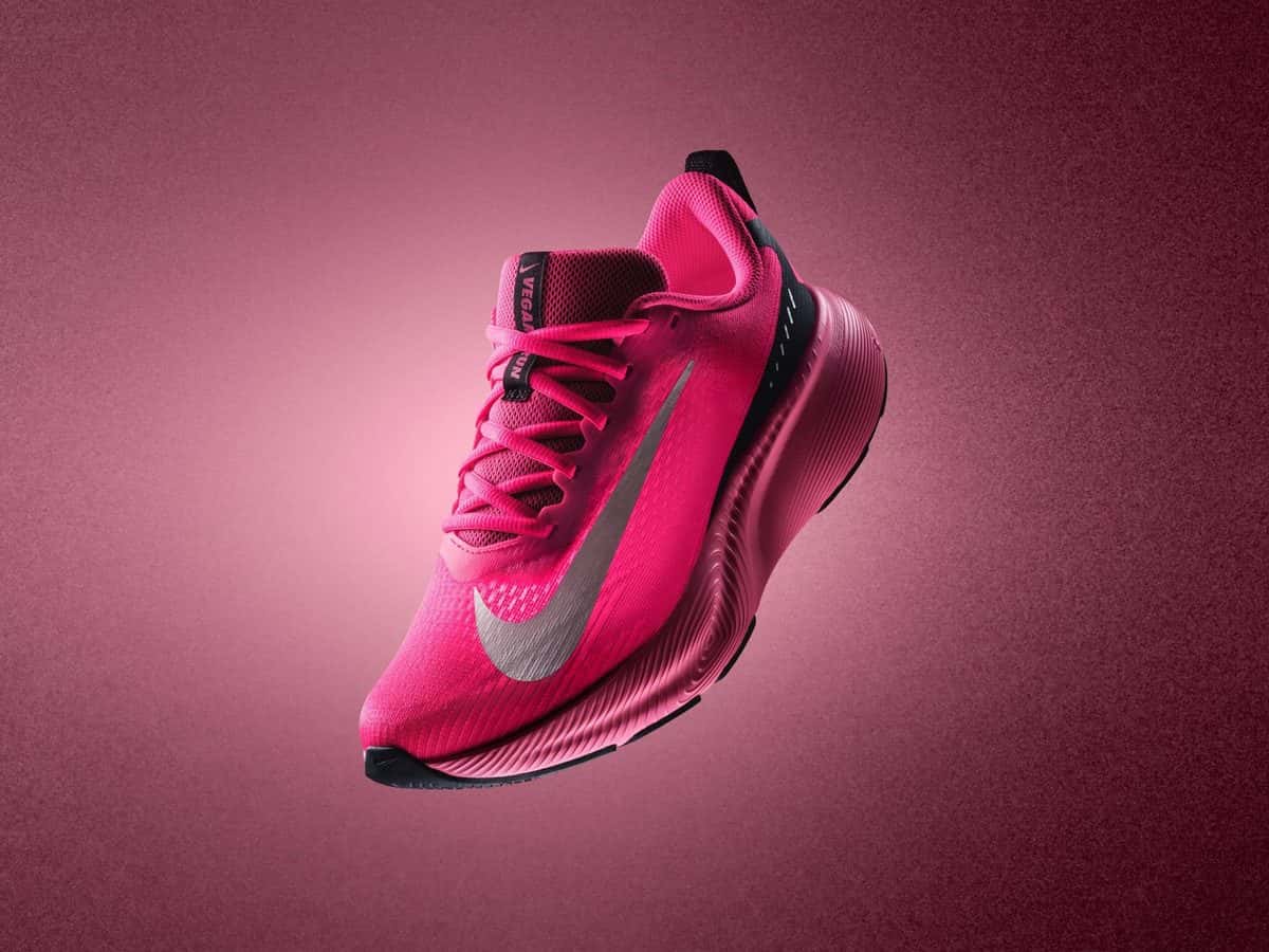 Nike Vegam Run en rosa fucsia con la pipa plateada, flotando sobre un fondo rosa oscuro