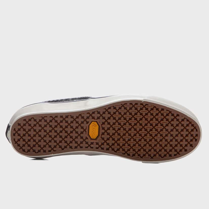 Suela de la OTW by Vans Era 95 Vibram Floral Black sobre fondo gris claro, en caucho marrón con dibujo geométrico de cruces y el logo octogonal amarillo de Vibram en el centro, rodeada por el borde blanco