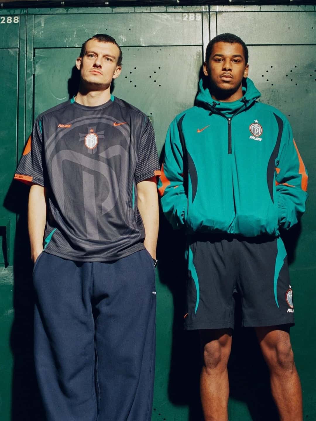 Dos personas con ropa de la colección Palace x Nike Manor Place FC: una camiseta gris con el escudo y una campera verde azulado con bermuda, frente a unos lockers verdes