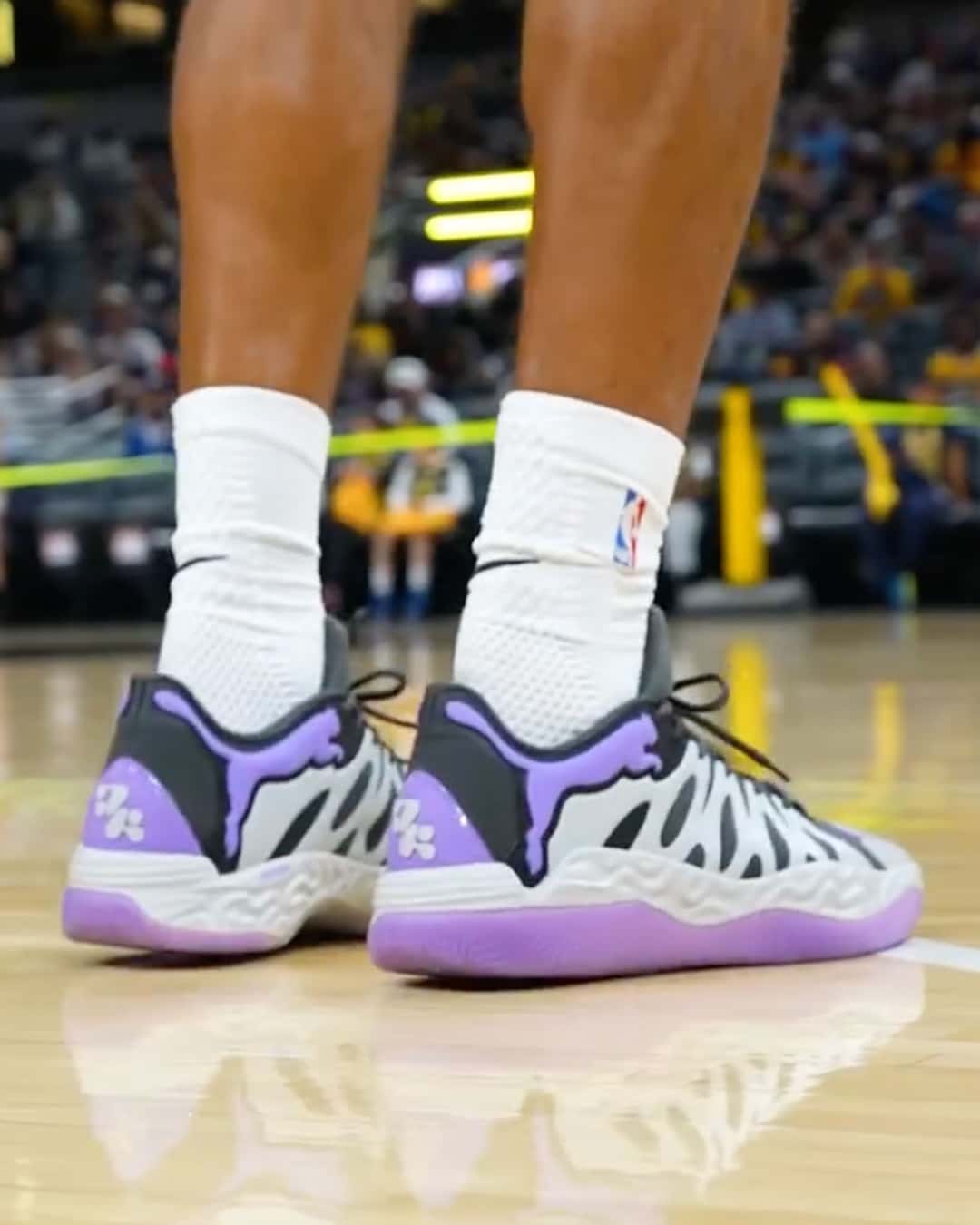 Vista trasera de las PUMA Hali 1 Teddy Lockart puestas en la cancha, con el clip del talón violeta y el logo de Haliburton, el felino de PUMA violeta sobre fondo negro y la suela violeta