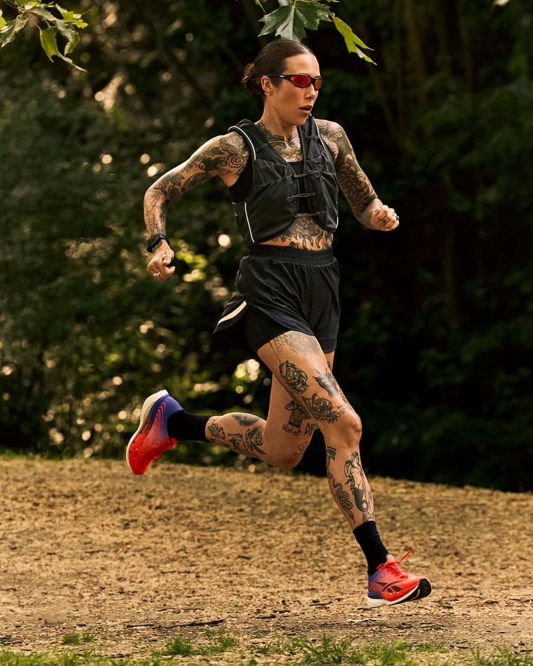 Corredora en plena zancada en un sendero de tierra entre árboles, con musculosa de hidratación negra y las Reebok SpeedShifter en naranja y azul