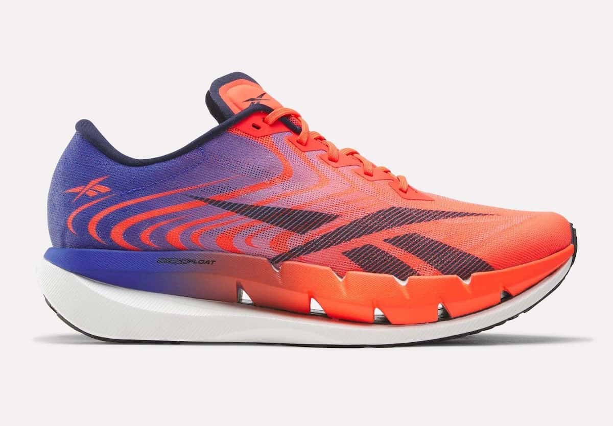 Reebok SpeedShifter de perfil lateral sobre fondo claro, con upper en degradé de naranja rojizo a azul violeta, vector Reebok azul marino y mediasuela blanca con el borde naranja