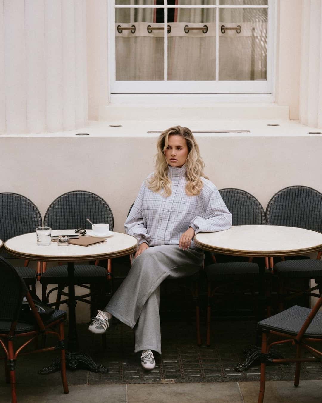 Molly-Mae sentada en la vereda de un café con las adidas Samba Slate y un conjunto gris, en una foto de la campaña de adidas