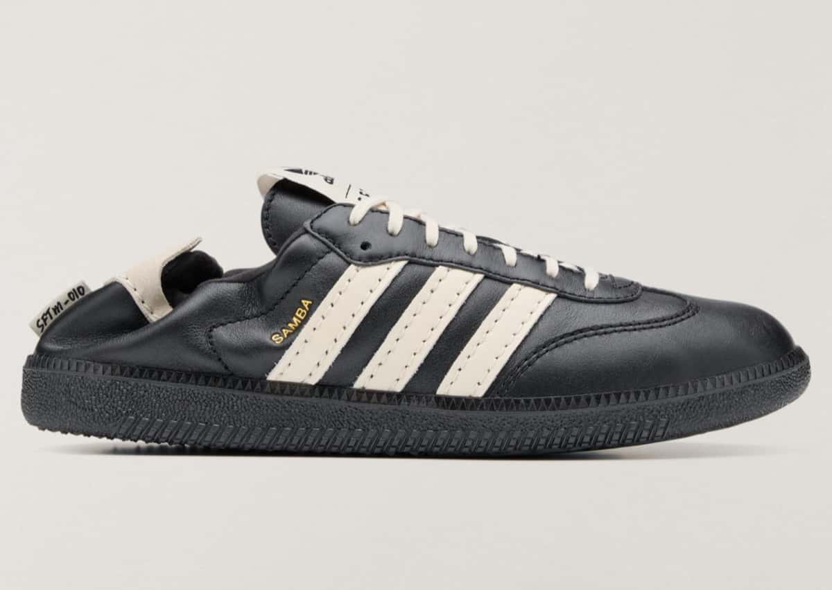 Vista lateral del adidas Samba OG de Song for the Mute en cuero negro con las tres tiras en cuero crema, la palabra Samba en dorado, cordones crema, suela negra y el talón hundido hacia adentro con una etiqueta que dice SFTM-010, sobre fondo gris claro