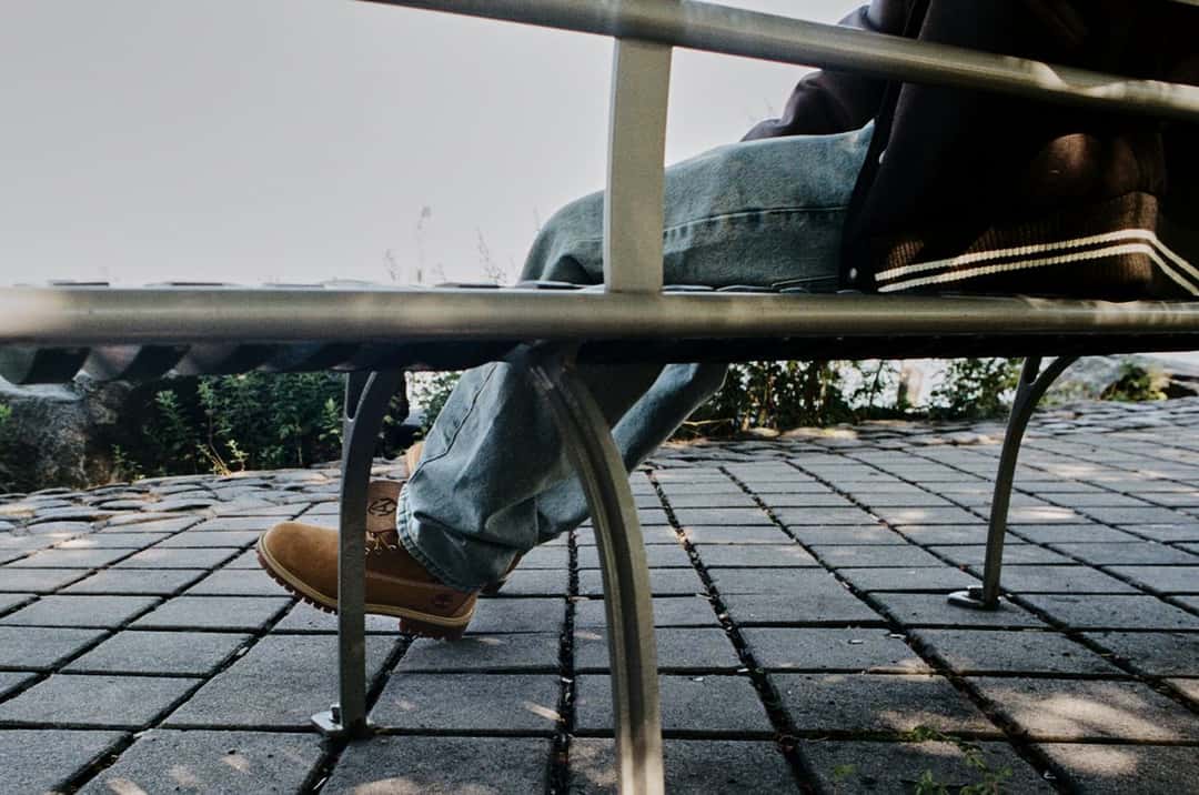 Detalle de una bota Timberland de Slam Jam apoyada en el piso de baldosas, debajo de un banco de metal