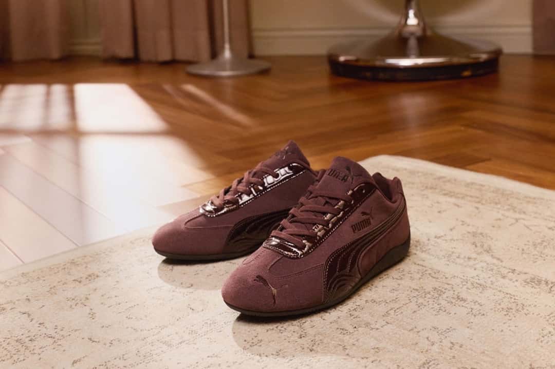 Par de PUMA Speedcat Croc marrón oscuro apoyado sobre una alfombra en un living con piso de madera, de la campaña de lanzamiento