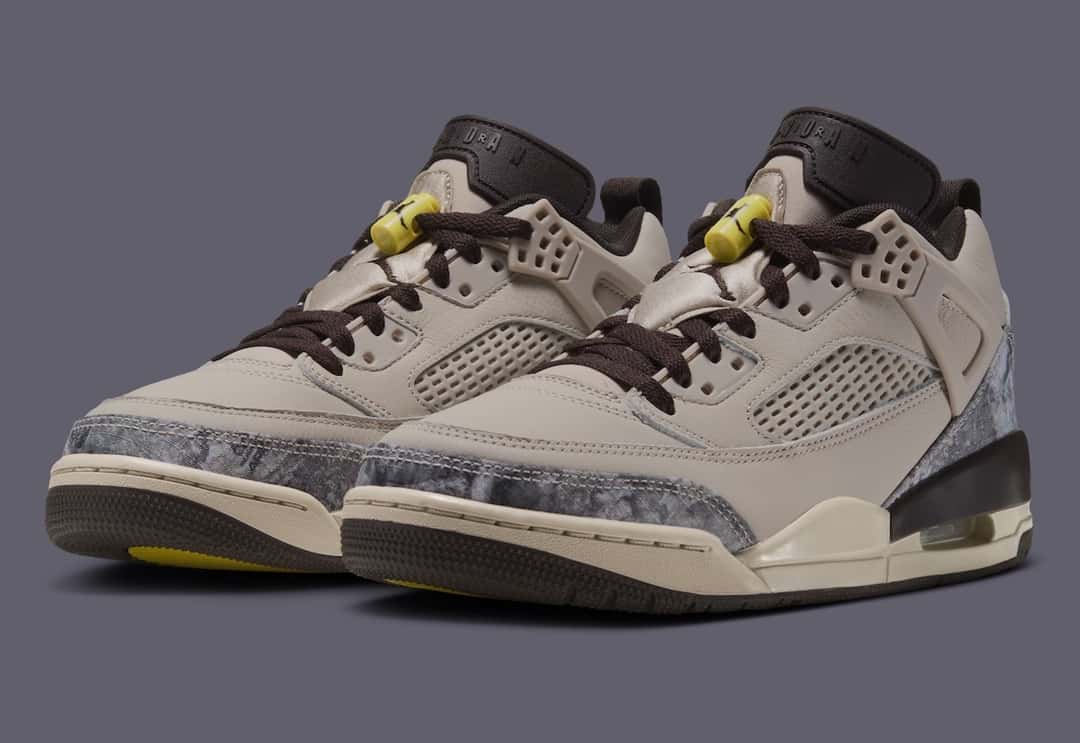 Par del Jordan Spizike Low Realtree Camo en tres cuartos sobre fondo gris, con upper crema, camuflaje gris en la punta, cordones marrón oscuro, traba de cordones amarilla y una burbuja de aire visible en el talón