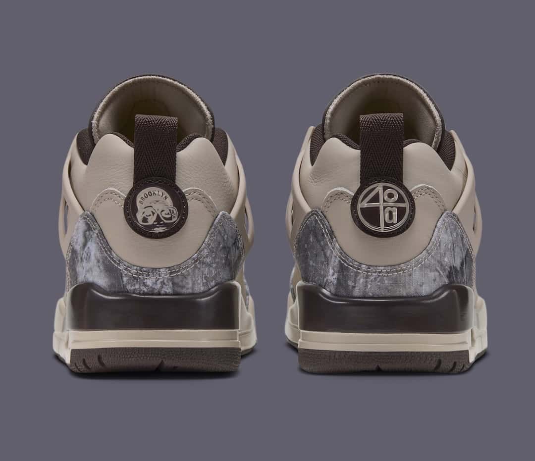Vista trasera del par del Jordan Spizike Low Realtree Camo, con tiradores marrón oscuro, una insignia circular con la palabra Brooklyn en un talón y otra con el número 40 en el otro, sobre el camuflaje gris del contrafuerte