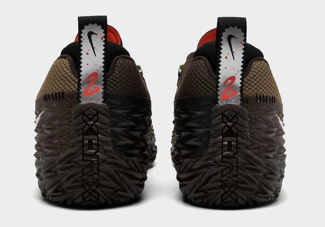 Talones del par de Nike ST Charge Halloween de Cade Cunningham sobre fondo gris claro, con tiradores plateados de borde dentado, el Swoosh negro y el número 2 en rojo rodeado de gotas rojas, y la goma texturada marrón con salpicado negro