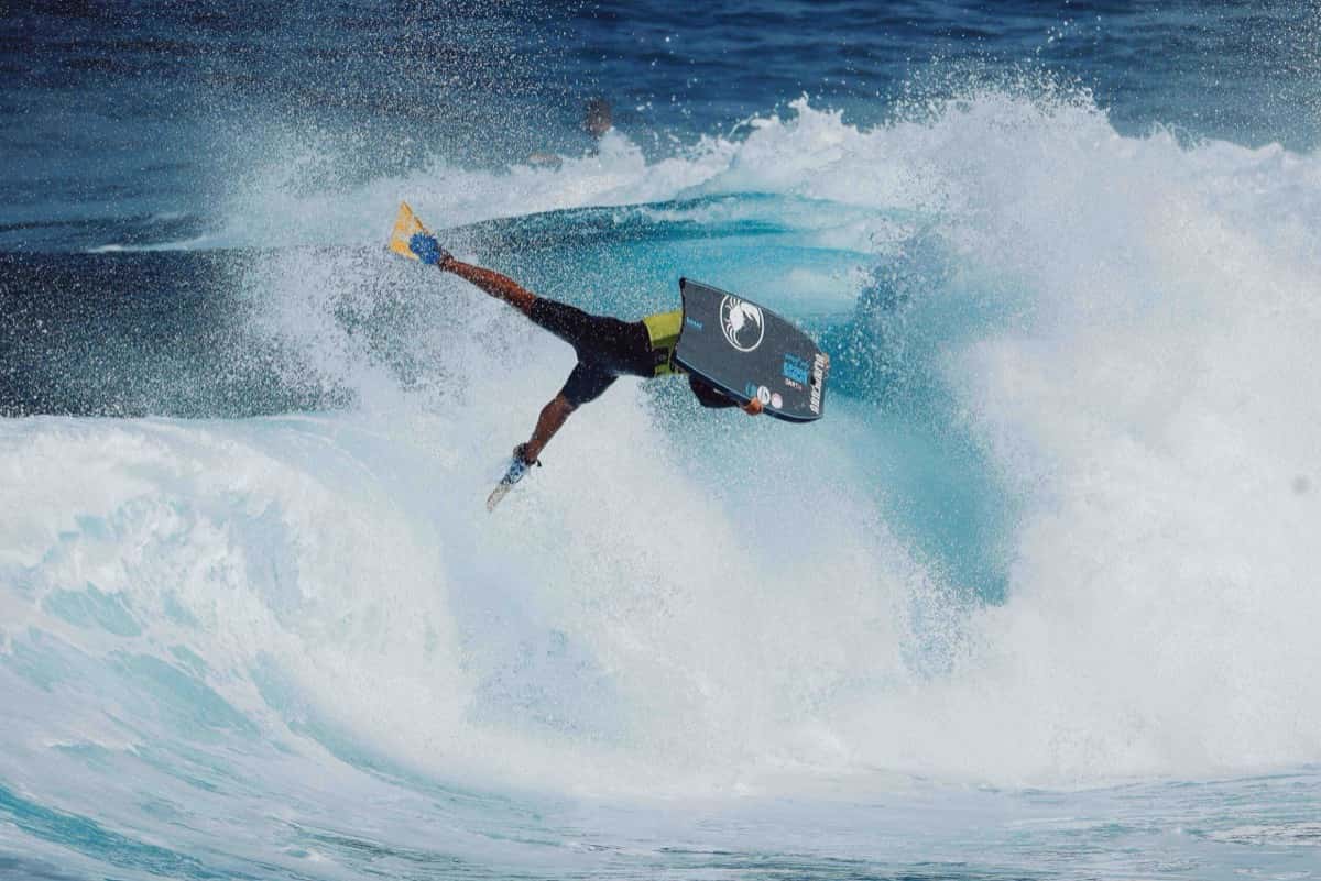 Un bodyboarder con aletas amarillas y tabla gris hace una maniobra invertida en la espuma de una ola en El Frontón, Gran Canaria, durante la quinta jornada del Frontón King 2026